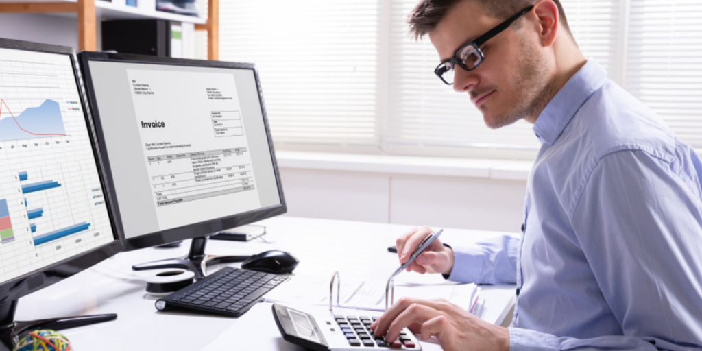 A person sat at a desk using a calculator, with several computer monitors around them.