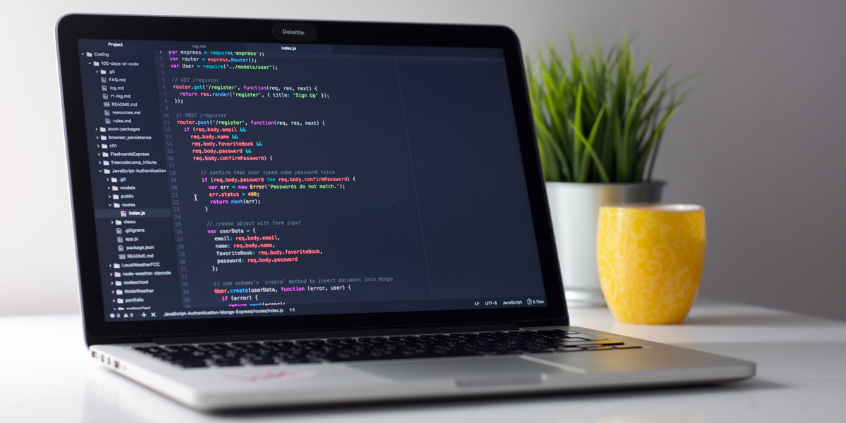 Laptop sits on a white desk with coding on its screen.