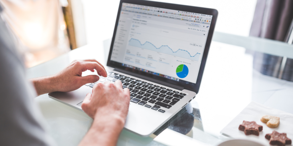 An open laptop showing a pie and line graph on the screen. A digital marketer is typing on the keyboard