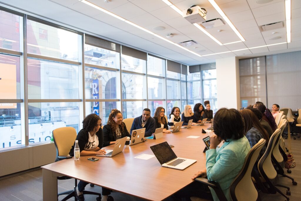 A bright office meeting room. A group of people sitting around a board room table with smiles on their faces. 