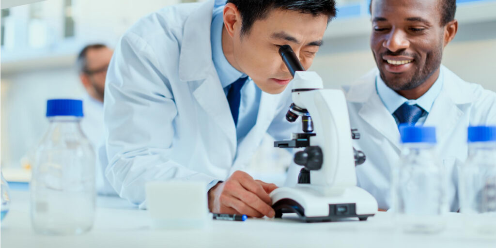 Man looking into a microscope with his colleague