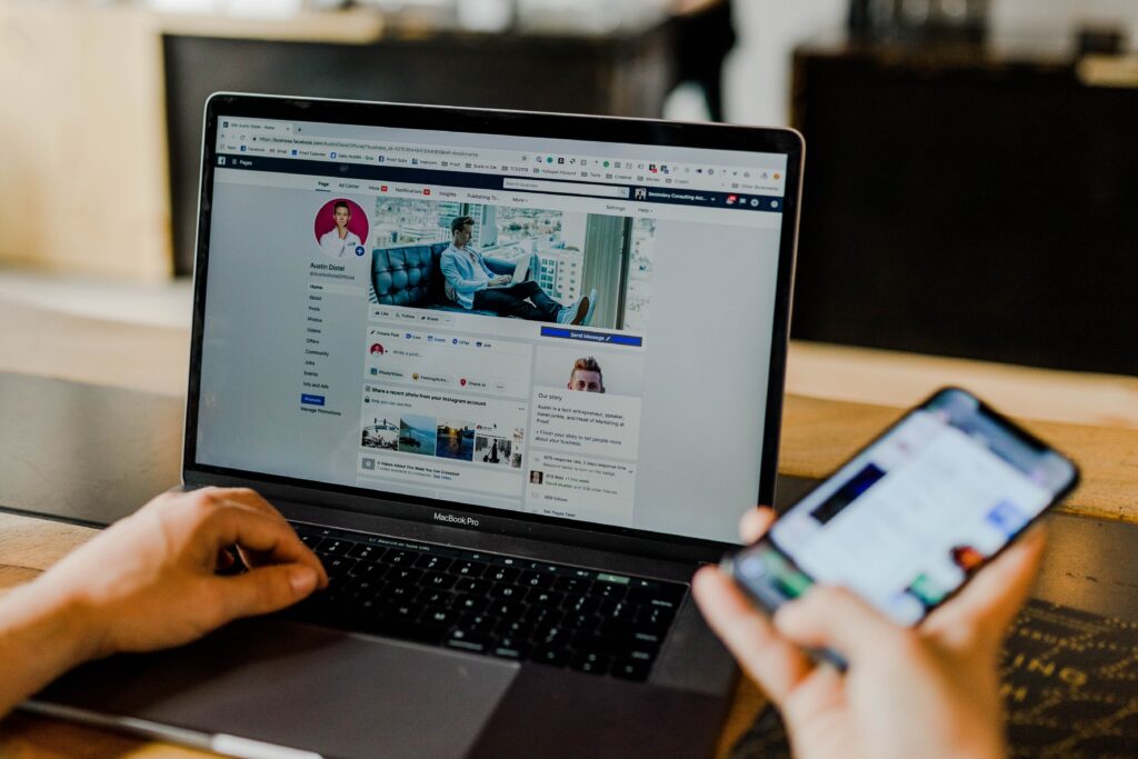 A person holding a laptop and phone, showing social media profiles.