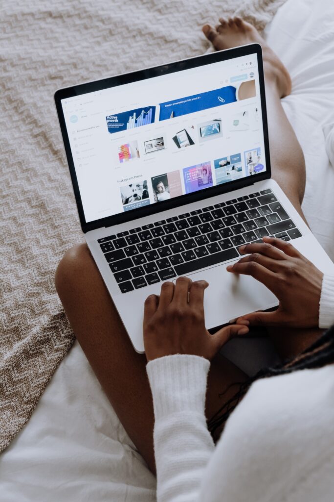 Woman on Canva, a great Digital Marketing tool which helps you design content. The laptop is silver and she is currently choosing a template while laying on her bed.