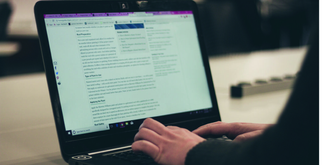 Two hands typing on a laptop, creating a blog post on the screen.