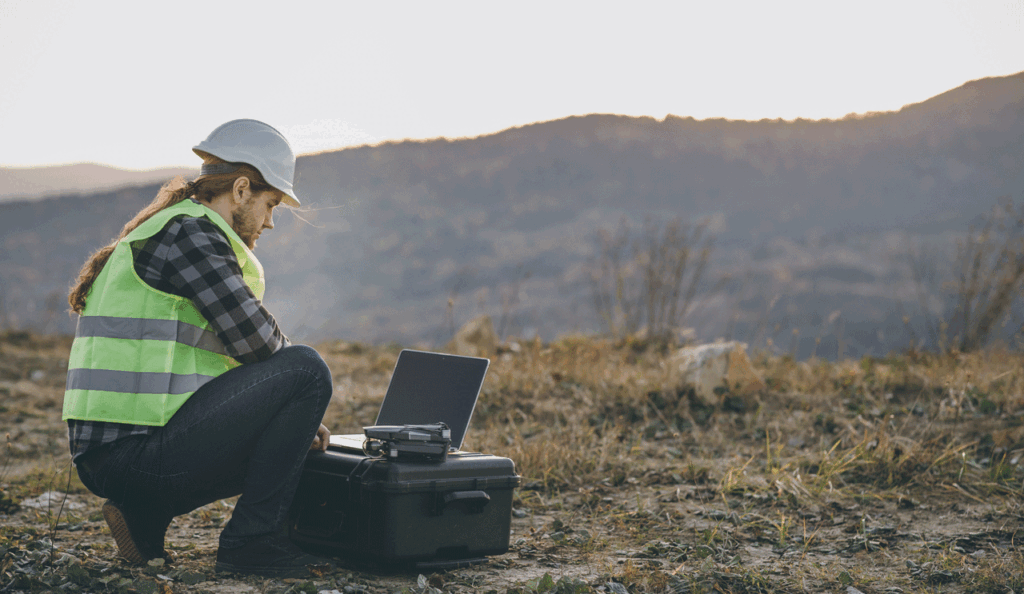 Landscape technician in the helmet Uses Touchscreen against open outdoor  hilly backdrop