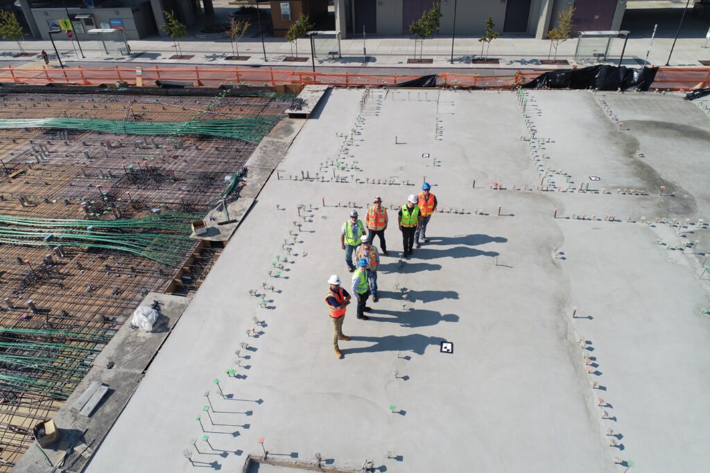 Aerial view of a group of construction site supervisors wearing safety gear, standing in the centre of an empty construction site.
