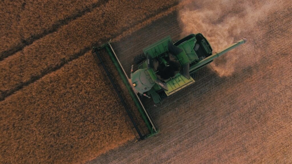 image shows a tractor in a field harvesting wheat from an aerial perspective