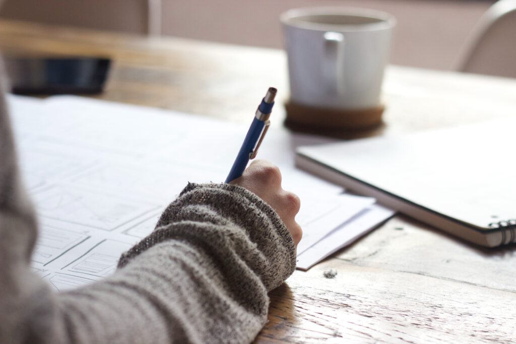 Person writing on brown wooden table near white ceramic mug. apprenticeships, space systems engineering