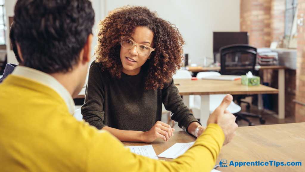 Level 3 Assistant Accountant Blog Post Embedded Image showing two people talking in an office with documents on the table and one of them giving a thumbs up.